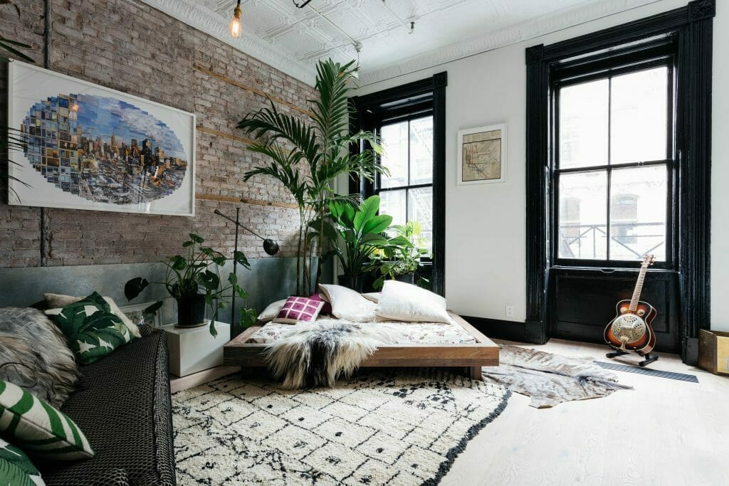 przestronna sypialnia styl loftowy, łóżko z palet, ceglana ściana, palmy i duże rośliny
