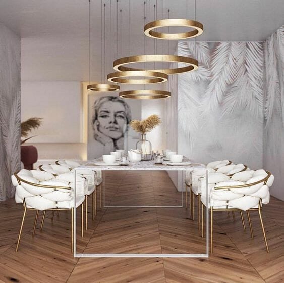 lampy do salonu w postaci złotych obręczy nad stołem jadalnianym