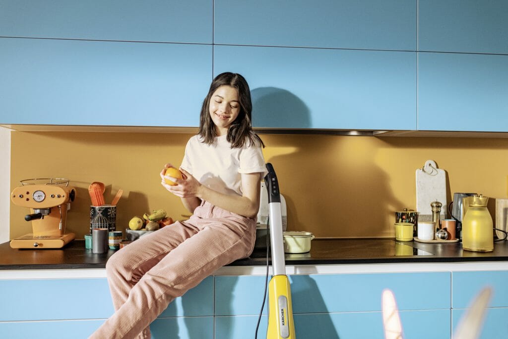 młoda dziewczyna siedzi na blacie w kuchni z szafkami z niebieskimi frontami
