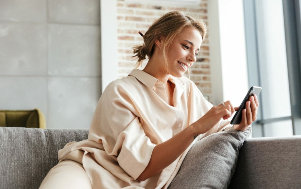 Kobieta na kanapie włącza pralkę Midea MF200 za pomocą aplikacji w smartfonie