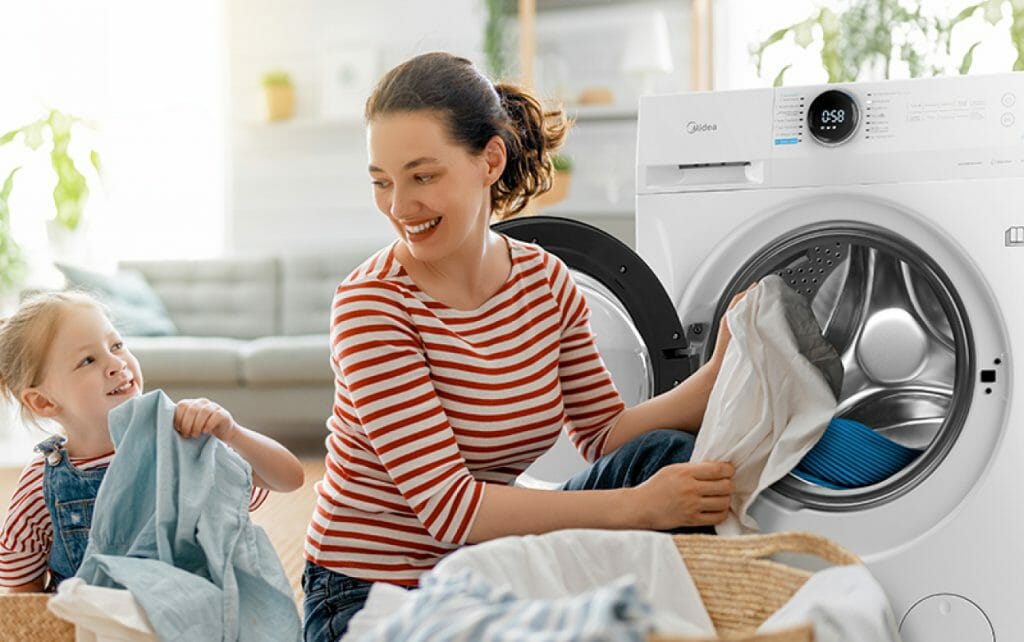 Uśmiechnięta kobieta razem z córką wyjmuje pranie z pralki Midea MF200